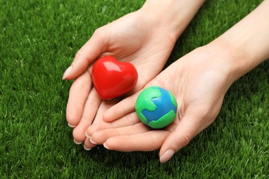 Happy Earth Day. Woman with plasticine planet and decorative heart on green grass, closeup