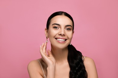 Young woman wearing elegant pearl earrings on pink background