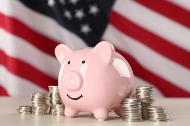 Piggy bank and coins on white wooden table against American flag