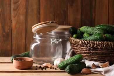 Photo of Fresh cucumbers and other ingredients near empty jars prepared for canning on wooden table. Space for text
