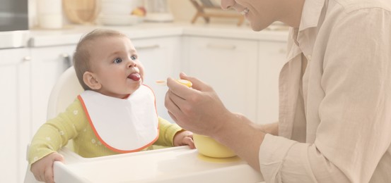 Father feeding his cute little baby in kitchen. Banner design