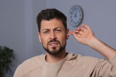 Photo of Emotional man cleaning ears and suffering from pain in room