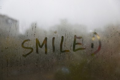 Word SMILE written on foggy window. Rainy weather