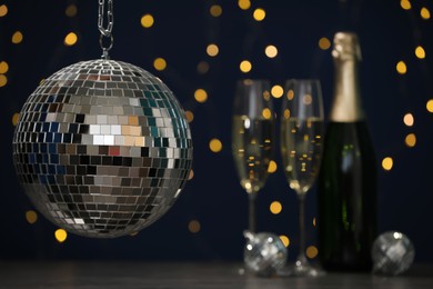 Shiny disco ball hanging over table with champagne against blurred lights, space for text