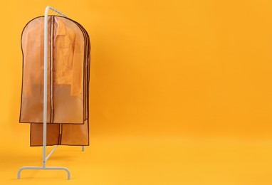 Garment bags with clothes on rack against yellow background. Space for text