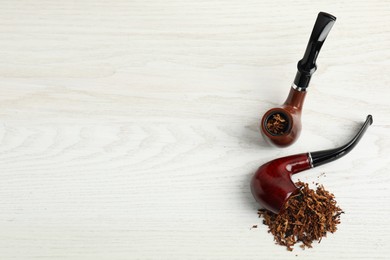 Smoking pipes with tobacco on white wooden table, flat lay. Space for text