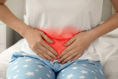 Woman suffering from abdominal pain on bed at home, closeup
