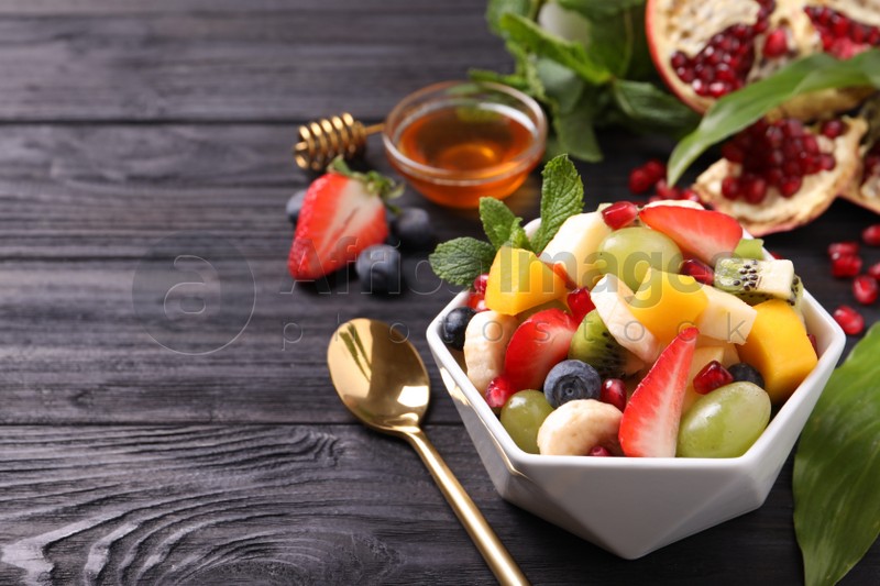Delicious fresh fruit salad in bowl on black wooden table, space for text
