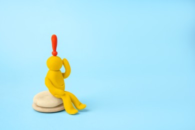 Photo of Human figure made of yellow plasticine with exclamation mark as solution idea on light blue background. Space for text
