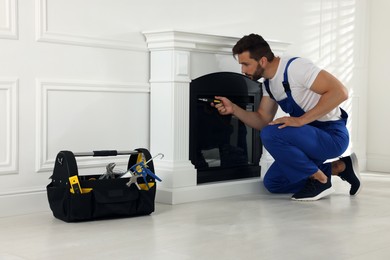 Photo of Professional technician with screwdriver installing electric fireplace in room