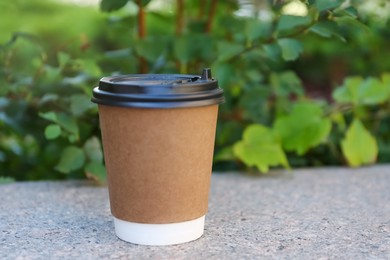Disposable paper cup with plastic lid on stone parapet outdoors, space for text