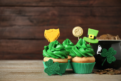 Decorated cupcakes and pot with gold coins on wooden table. St. Patrick's Day celebration