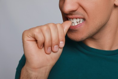 Man biting his nails on grey background, closeup. Bad habit