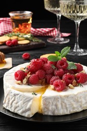 Brie cheese served with raspberries and walnuts on black plate, closeup