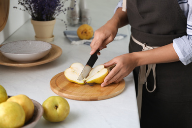 Woman cutting fresh ripe pear at table in kitchen, closeup