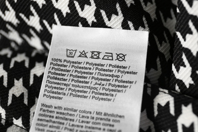 Clothing label with care symbols and material content on shirt, closeup view