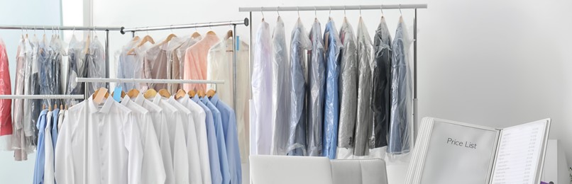Racks with clean clothes on hangers indoors, banner design. Dry-cleaning service