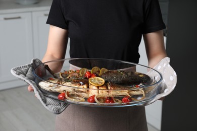 Photo of Woman holding baking tray with sea bass fish and garnish, closeup