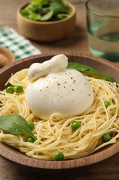 Photo of Bowl of delicious pasta with burrata, peas and spinach on wooden table, closeup