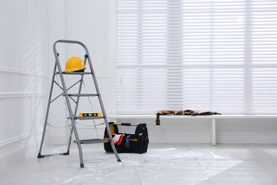 Photo of Metal stepladder with hardhat, level and toolkit indoors