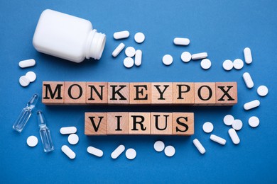 Words Monkeypox Virus made of wooden cubes, vials and pills on blue background, flat lay