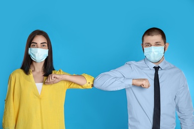 Man and woman bumping elbows to say hello on light blue background. Keeping social distance during coronavirus pandemic