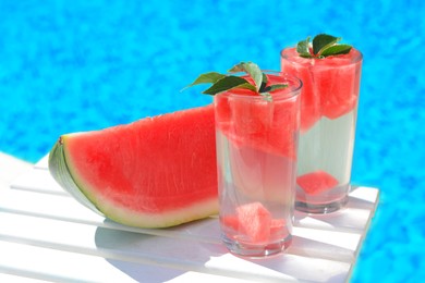 Refreshing drink in glasses and sliced watermelon near swimming pool outdoors