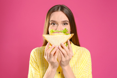 Photo of Young woman eating tasty sandwich on pink background