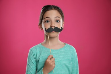 Photo of Cute little girl with fake mustache on pink background