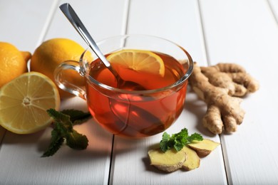 Cup of delicious ginger tea and ingredients on white wooden table, closeup