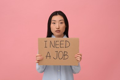 Photo of Unemployed Asian woman holding sign with phrase I Need A Job on pink background