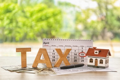 Word TAX, calendar and model of house on table