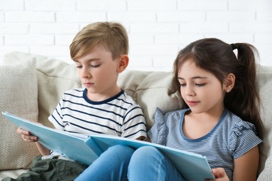 Little boy and girl reading book on sofa at home