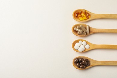 Wooden spoons with different dietary supplements on white background, flat lay. Space for text