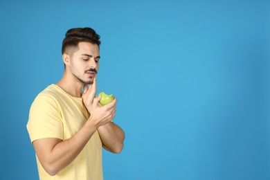 Young man with sensitive teeth and apple on color background. Space for text