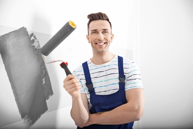 Young male decorator painting wall in room