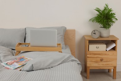 Wooden tray table with laptop and smartphone on bed indoors