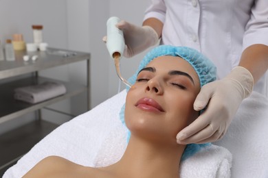 Photo of Young woman undergoing face rejuvenation procedure with darsonval in salon