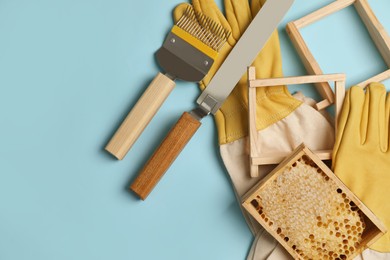 Photo of Hive frame with honeycomb and beekeeping equipment on light blue background, flat lay