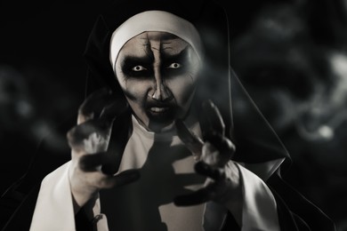 Photo of Portrait of scary devilish nun and smoke on black background. Halloween party look