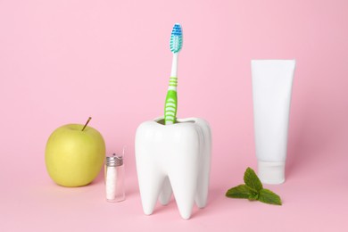 Tooth shaped holder with toothbrush, paste and apple on pink background