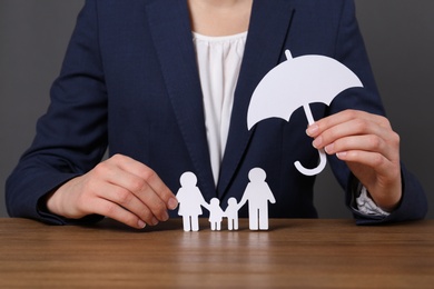 Woman holding cutout paper family and umbrella at table, closeup. Life insurance concept