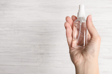 Photo of Woman holding antiseptic spray on light background, closeup. Space for text