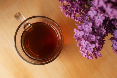 Photo of Beautiful lilac flowers and glass cup of tea on wooden table, top view