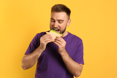 Photo of Young man eating tasty sandwich on yellow background