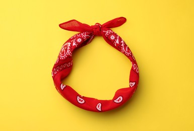 Tied red bandana with paisley pattern on yellow background, top view
