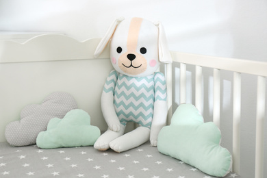 Cute toy dog and cloud shaped pillows in crib, closeup. Baby room interior elements