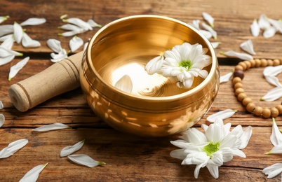 Golden singing bowl with flower and mallet on wooden table, closeup. Sound healing
