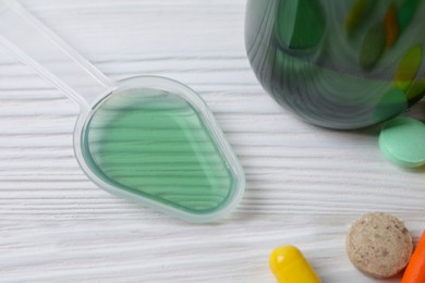 Photo of Plastic dosing spoon with syrup and pills on white wooden table, closeup. Cold medicine