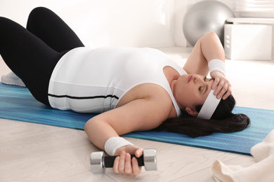 Lazy overweight woman resting instead of training on mat at gym